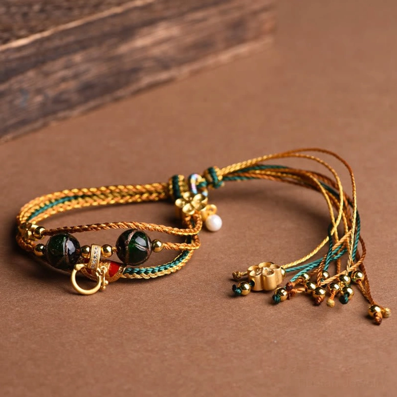 Single Tibetan liuli glass healing bracelet side view on brown background showing multi-strand braided rope construction with dark green beads and metal flower charm