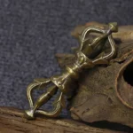 Handcrafted five-prong tibetan vajra dorje in antique brass copper, overhead view on weathered wood with dark fabric background, showing intricate carved details of sacred ritual implement