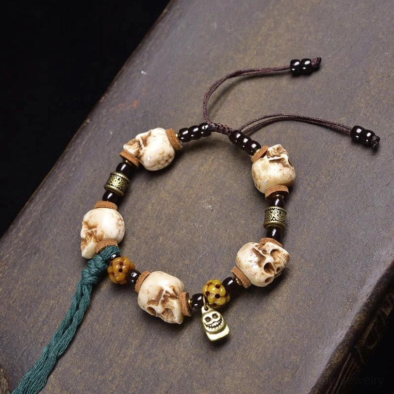 Multi-skull bone bead bracelet featuring five bone skulls with metal beads and green tassel accent