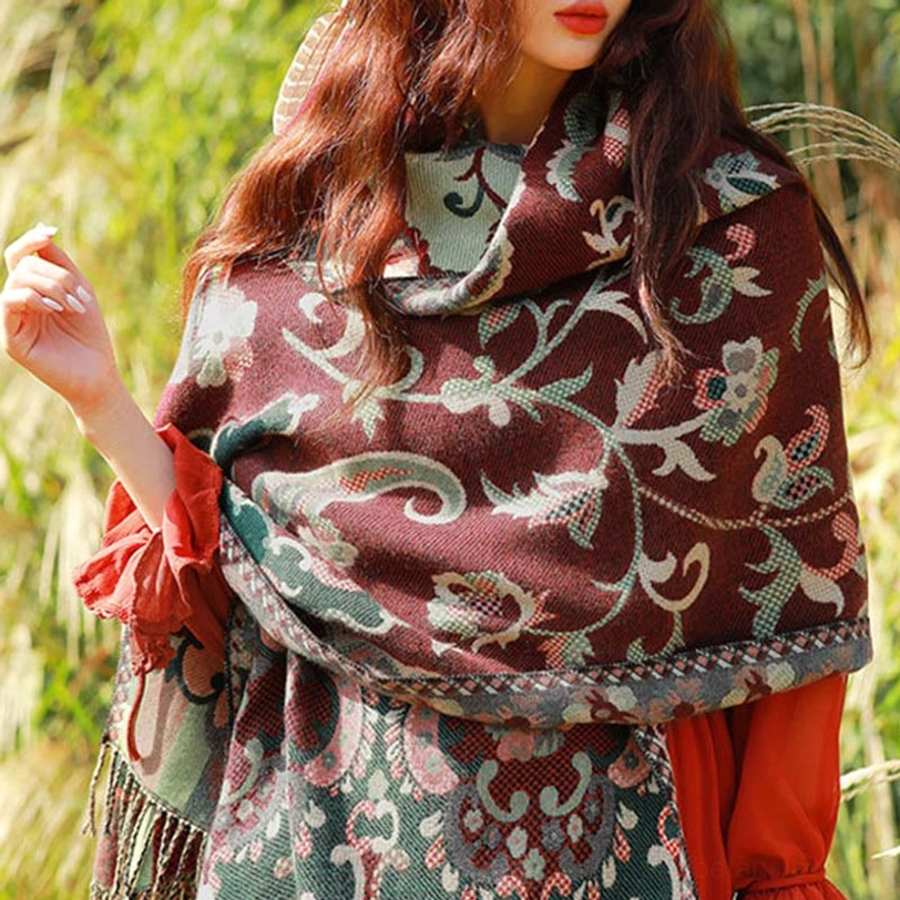 Tibetan ethnic floral paisley tassel shawl in maroon with green floral patterns, front three-quarter view in reed grass field