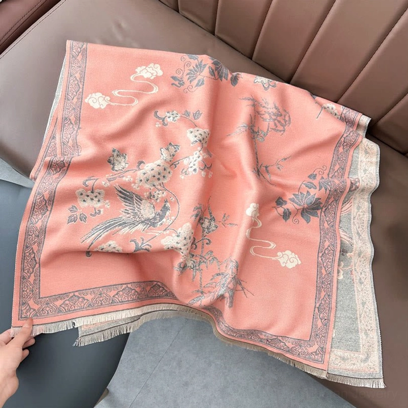 Light pink handwoven Tibetan scarf laid on sofa showing intricate bird and flower print with fringed edge