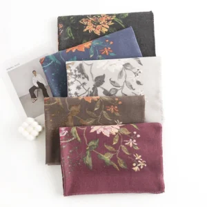 Collection of Tibetan floral scarves in multiple colorways arranged on flat lay desktop with fashion magazines, featuring rich jewel tones and earth-toned botanical motifs