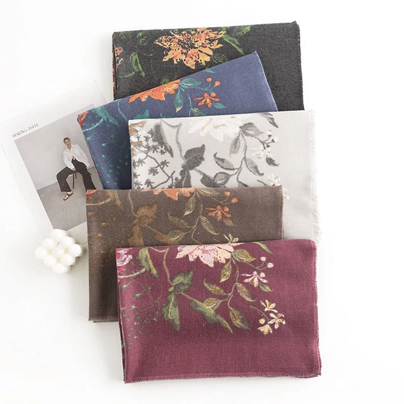 Collection of Tibetan floral scarves in multiple colorways arranged on flat lay desktop with fashion magazines, featuring rich jewel tones and earth-toned botanical motifs
