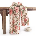 Tibetan floral shawl with pink flowers and green leaves, draped on vintage wooden table, beige soft fabric perfect for fall and winter layering