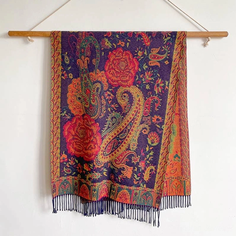 Flat lay floral shawl hung on wooden rod, front view showcasing all-around fringed hem and intricate ethnic pattern