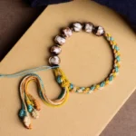 Handmade Tibetan multicolor liuli glass bead fortune bracelet with braided rope on kraft paper, flat lay top-down view showing all five element colors