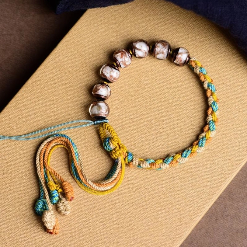 Handmade Tibetan multicolor liuli glass bead fortune bracelet with braided rope on kraft paper, flat lay top-down view showing all five element colors