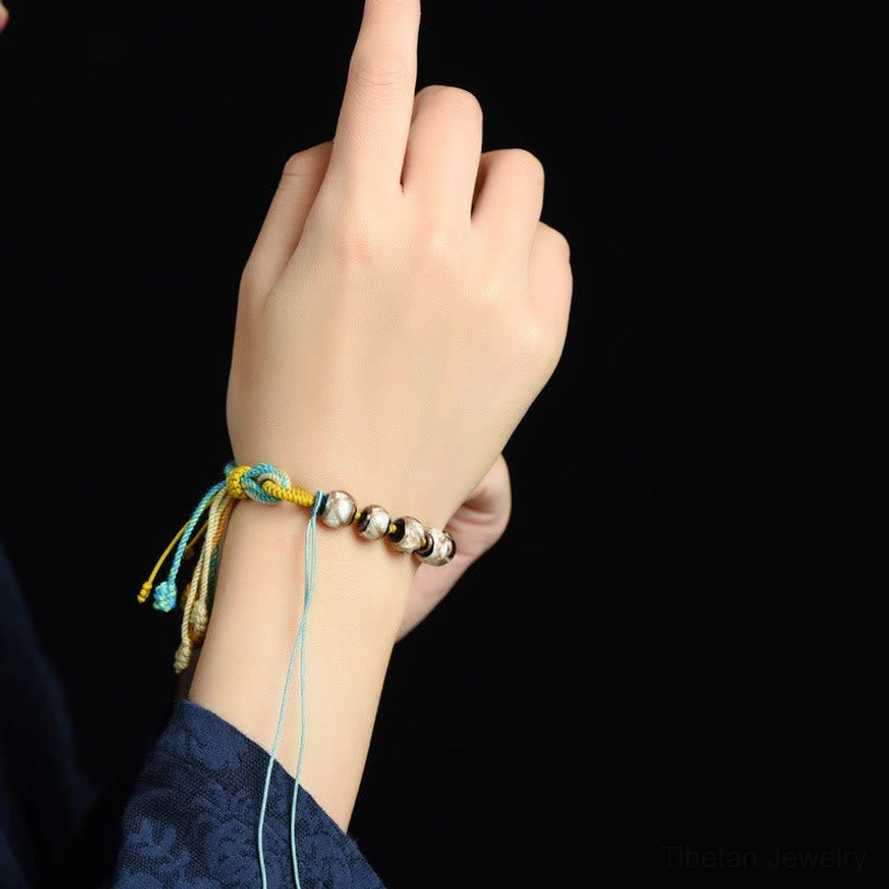 Wearing demonstration of Tibetan liuli glass bead bracelet on wrist, close-up shot showing silver round beads and colored braided rope in actual use