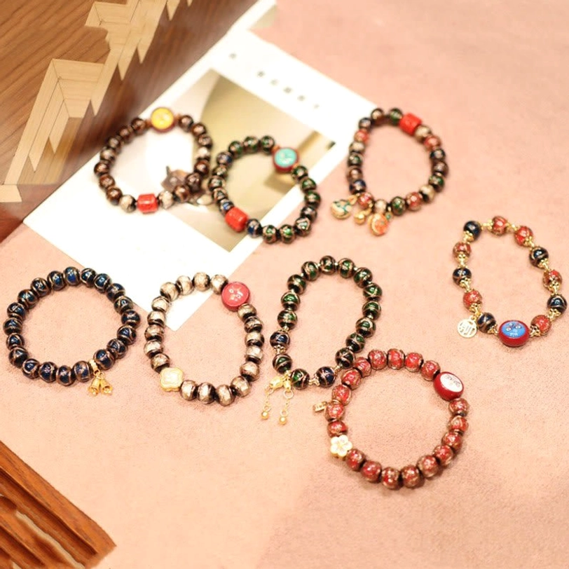 Assorted Tibetan fortune bracelets with various color schemes, gold tone pendants and elastic beaded bands on wooden surface