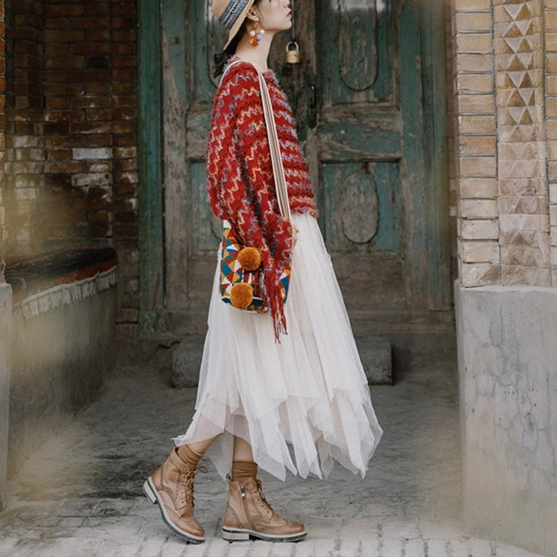 Fringed tibetan knit travel shawl with asymmetric tassel hem shown from back view paired with ankle boots in vintage yard