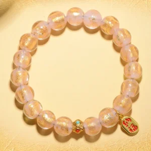 Gold liuli glass bead bracelet with fu character pendant and enamel spacers flat lay on beige background