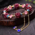 Tibetan garnet amethyst healing bracelet with gold hardware and blue enamel accents displayed on wooden tray