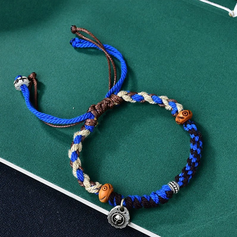 Blue Tibetan Garuda protection bracelet with hand-woven cord, wooden ox bone beads, and silver charm on dark green background