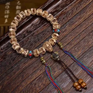 Close-up side view of Tibetan Garuda bone bracelet showing intricate carved bone beads, enamel accents, metal spacer beads, and multicolor tassel detail