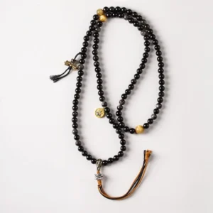 Flat lay studio shot of Tibetan Garuda obsidian protection necklace with braided tassel and metal charms