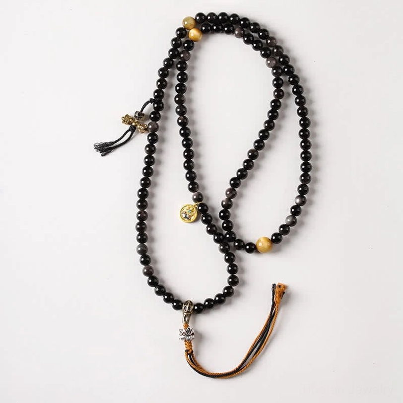 Flat lay studio shot of Tibetan Garuda obsidian protection necklace with braided tassel and metal charms