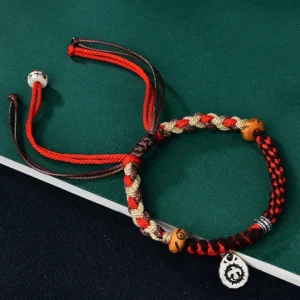 Red Tibetan Garuda protection bracelet with hand-woven cord, wooden ox bone beads, and engraved Tibetan silver charm on dark green tabletop
