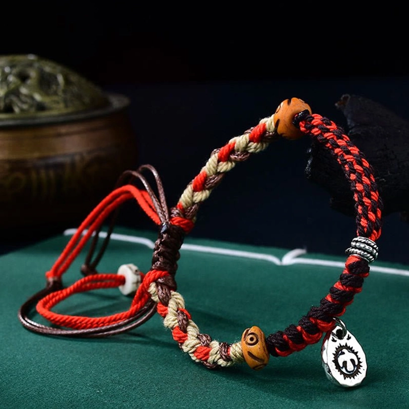 Red hand-woven Tibetan Garuda bracelet with adjustable cord ends and engraved metal ring charm