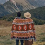 Tibetan geometric tribal blanket worn as outdoor poncho in mountain camping setting with warm earthy tones and fringed trim