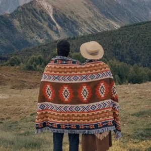 Tibetan geometric tribal blanket worn as outdoor poncho in mountain camping setting with warm earthy tones and fringed trim
