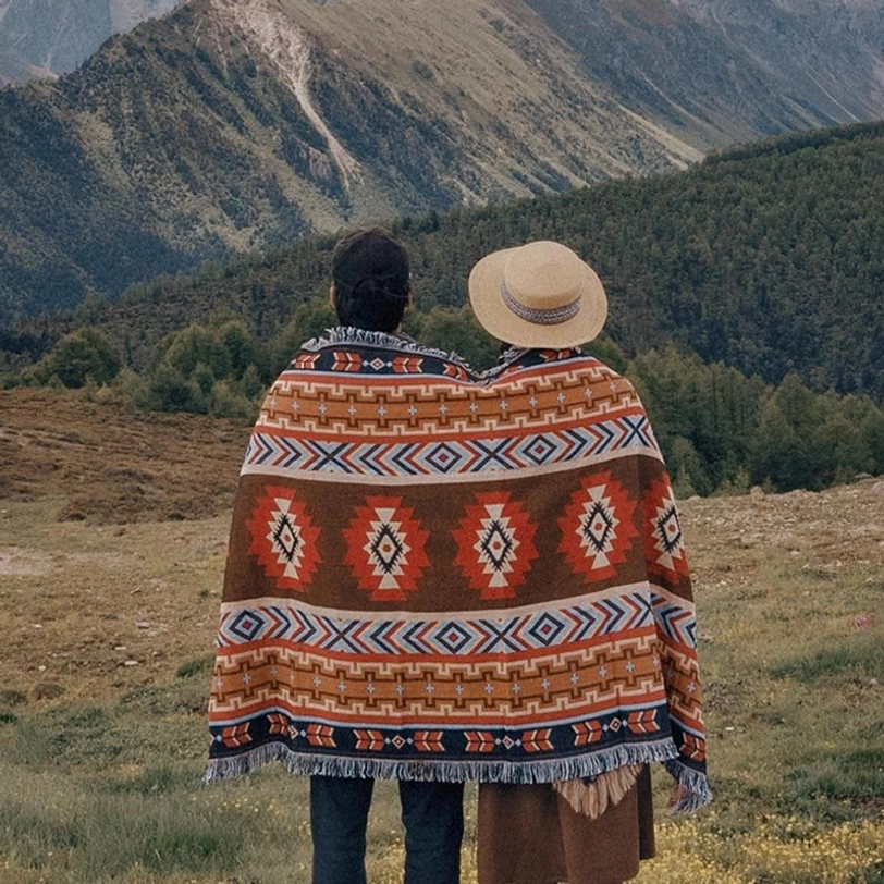Tibetan geometric tribal blanket worn as outdoor poncho in mountain camping setting with warm earthy tones and fringed trim
