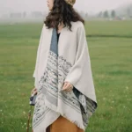 Tibetan geometric tassel shawl with blue beige patterns worn outdoors on grassy field, side view showing fringed tassel hem