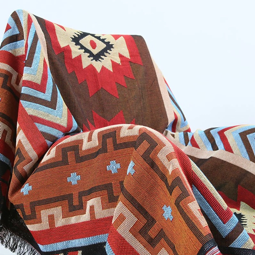 Hand-woven Tibetan geometric throw blanket in warm earth tones displayed on indoor chair