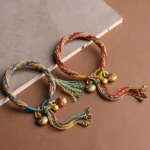 Tibetan gold beast family blessing bracelets with colorful woven cord, enamel monster charms and tassels on brown tabletop
