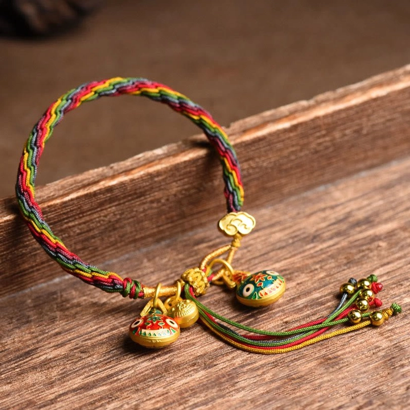 Tibetan gold swallowing beast family luck bracelet multicolor braided cord with enamel pendants and gold tassel details overhead view