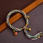 Tibetan gold swallowing beast family blessing bracelet with multicolor braided rope and three golden charms on dark wooden background