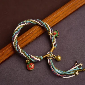 Tibetan gold swallowing beast family blessing bracelet with multicolor braided rope and three golden charms on dark wooden background