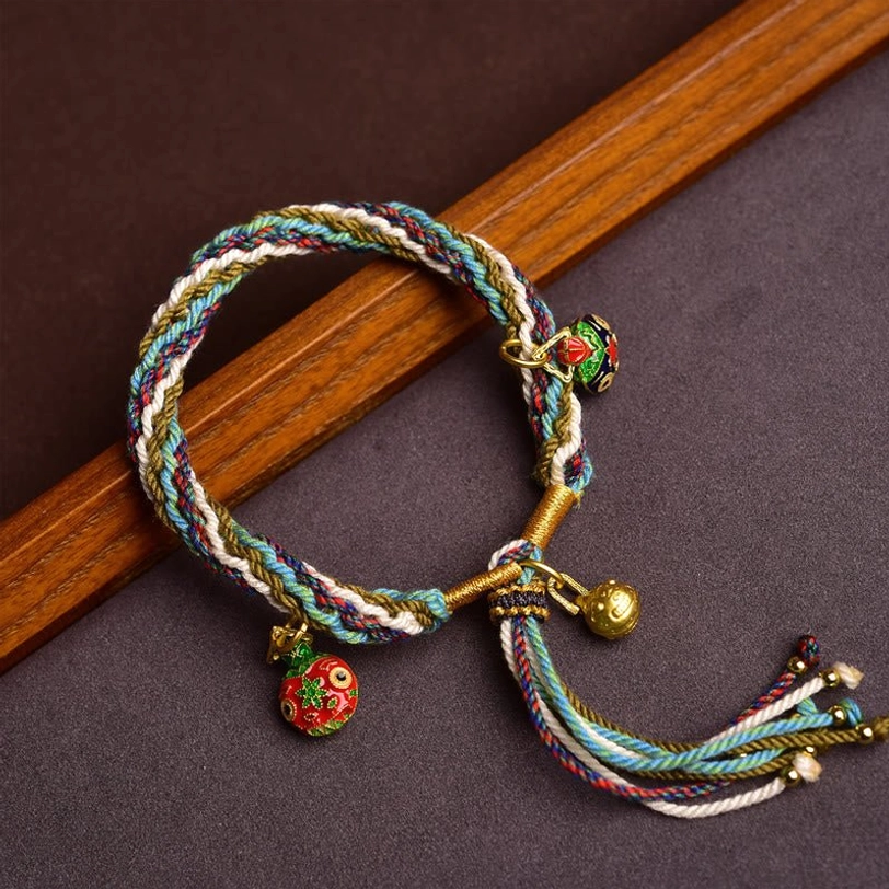 Tibetan gold swallowing beast family blessing bracelet with multicolor braided rope and three golden charms on dark wooden background