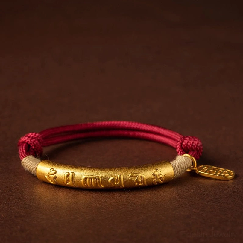 Gold-tube Tibetan braided bracelet with red cord and engraved six-word mantra on dark background