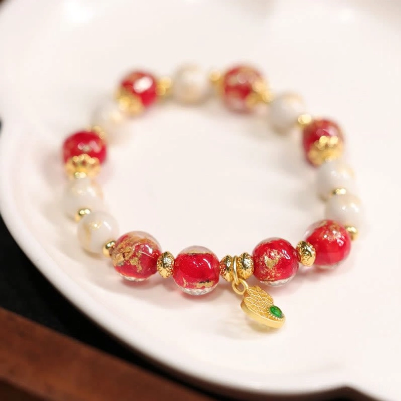 Tibetan god of wealth gourd bracelet with charm pendant positioned at lower right, incense ash and glass beads on white porcelain display plate