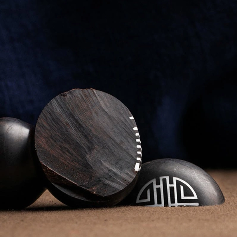 Unfinished ebony and sandalwood gourd-shaped ornaments with engraved double happiness pattern on dark blue fabric backdrop, side flat view showing raw wood texture