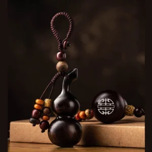Tibetan ebony gourd keychain with bead tassel on kraft paper packaging, front oblique view showing deep brown wood carving and double happiness ornament charm