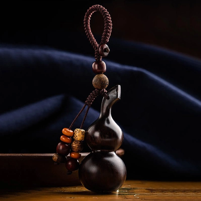 Handcrafted gourd-shaped keychain with multi-style wooden bead tassel against dark blue fabric, front three-quarter view highlighting fine artisan craftsmanship
