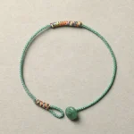 Green aventurine braided Tibetan luck bracelet with colorful woven accents and green donut pendant on gray background