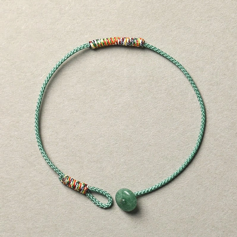 Green aventurine braided Tibetan luck bracelet with colorful woven accents and green donut pendant on gray background
