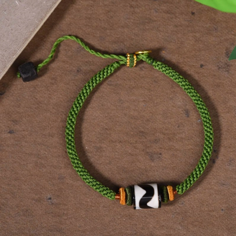 Full-length view of green braided dzi bead bracelet with black adjustable slider on wooden background