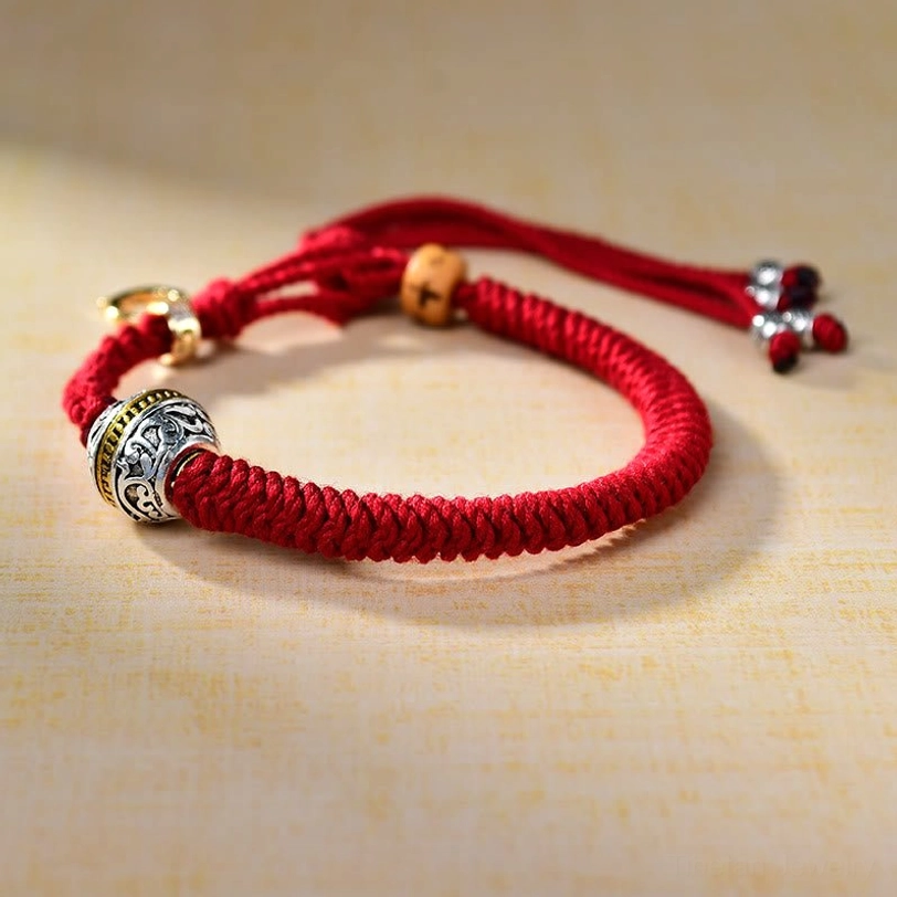 Red string Tibetan bracelet with Green Tara silver charm, wooden spacing bead, and gold-toned crystal tassel end close-up