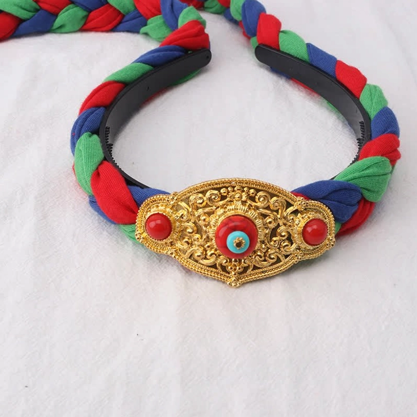 Close-up Tibetan hair accessory headband with braided multicolor bands and large gold carved ornament with inlaid gemstones