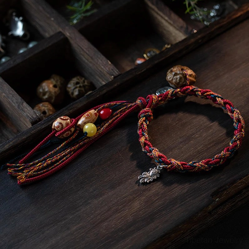 Hand-woven Tibetan protection bracelet with red mixed cord and silver leaf charm on wooden display box