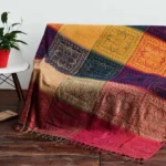 Tibetan handwoven damask throw blanket draped on wooden floor with geometric block pattern in warm earth tones