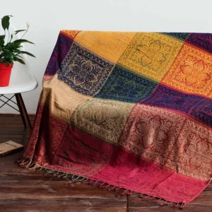 Tibetan handwoven damask throw blanket draped on wooden floor with geometric block pattern in warm earth tones