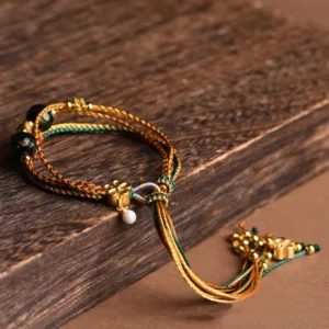 Handmade Tibetan healing bracelet flat lay on aged wooden surface, featuring mixed golden threads liuli glass beads and decorative flower clasp with tassel ornaments