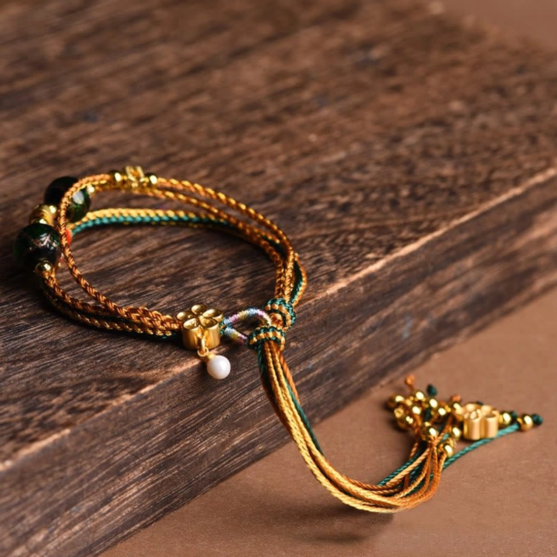 Handmade Tibetan healing bracelet flat lay on aged wooden surface, featuring mixed golden threads liuli glass beads and decorative flower clasp with tassel ornaments
