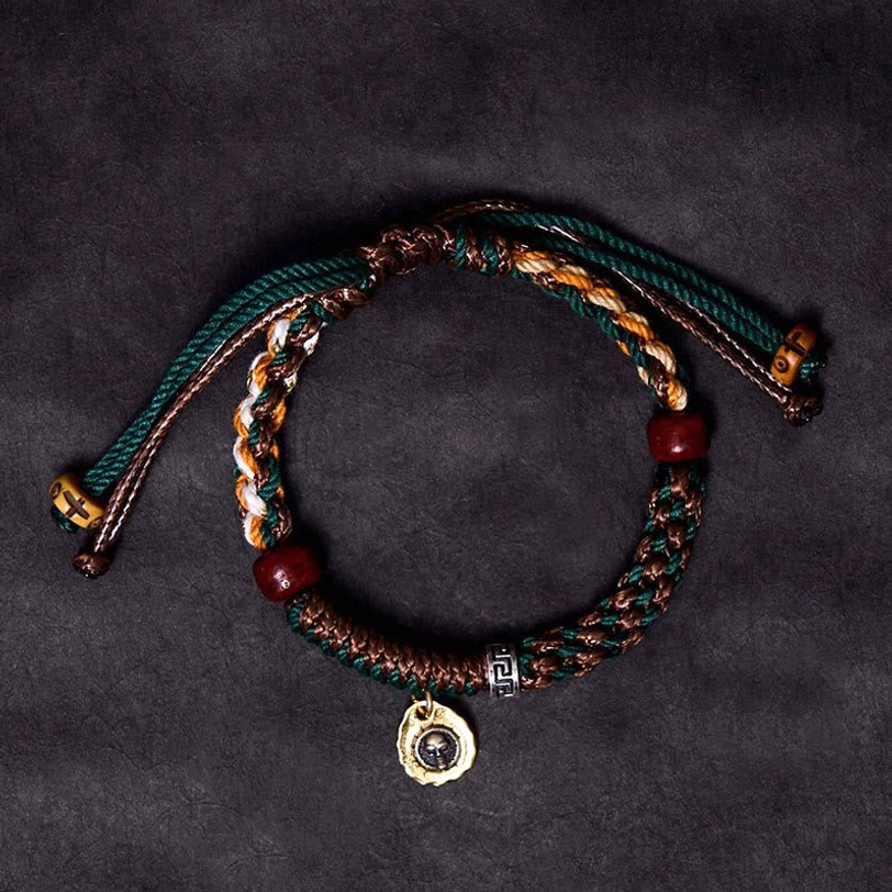 Tibetan braided rope bracelet with dark green and brown cords, red wooden beads, metal pendant on purple background