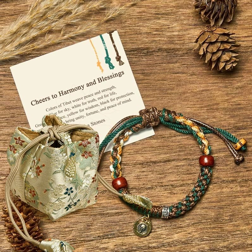 Tibetan rope bracelet with matching linen gift pouch and blessing card on wooden table with pinecones and wheat