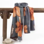Tibetan floral winter scarf with hibiscus print in dark gray and orange, displayed on vintage wooden furniture
